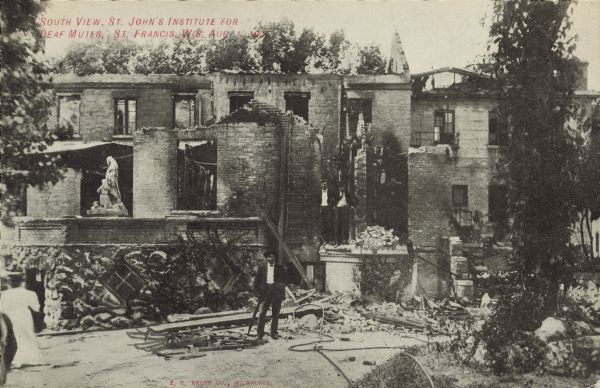 Text on front reads: "South View, St. John's Institute for Deaf Mutes, St. Francis, Wis. Aug. 1, 1907." A partially burned stone and brick building with people surveying the damage. A man is posing in the center and two men are standing on a platform. A statue is on the left. The fire began in the chapel roof, and no one was injured.