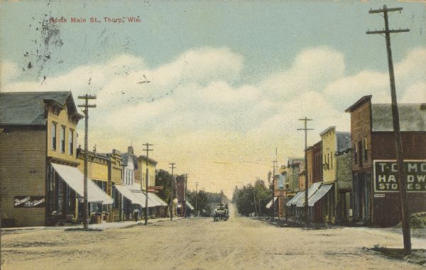 Text on front reads: "North Main St., Thorp, Wis." Storefronts with awnings line an unpaved street with paved sidewalks, a horse-drawn wagon travels down the center. 
