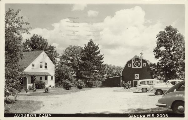 Text on front reads: "Audubon Camp, Sarona, Wis." A view of the headquarters buildings, house on the left, parked cars on the right, barn in the background, all surrounded by trees.