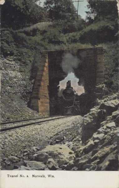 Text on front reads: "Tunnel No. 2, Norwalk, Wis." A locomotive is coming through a short tunnel, the sky can be seen on the other side. The entrance to the tunnel is built of square stone blocks. Trees and foliage are growing on the top.