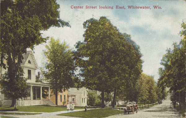 Text on front reads: "Center Street Looking East, Whitewater, Wis." Homes and trees on a street in a neighborhood. Passengers in an automobile are parked in front of a white house with children on the sidewalk.