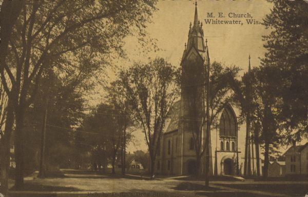Text on front reads: "M.E. Church, Whitewater, Wis." A stone church with an ornate steeple on a tree-lined street.