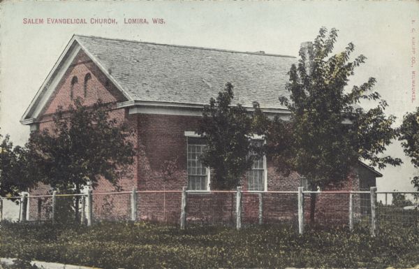 Text on front reads: "Salem Evangelical Church, Lomira, Wis." A brick, one-story church inside a fenced yard with trees.
