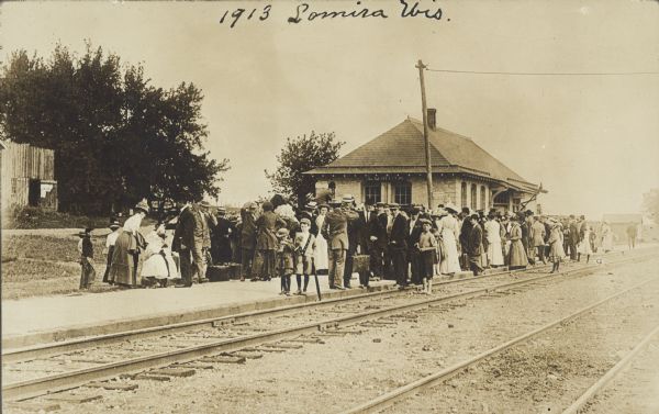 Handwriting on front reads: "1913 Lomira, Wis." A crowd of women and children waiting at a train station.