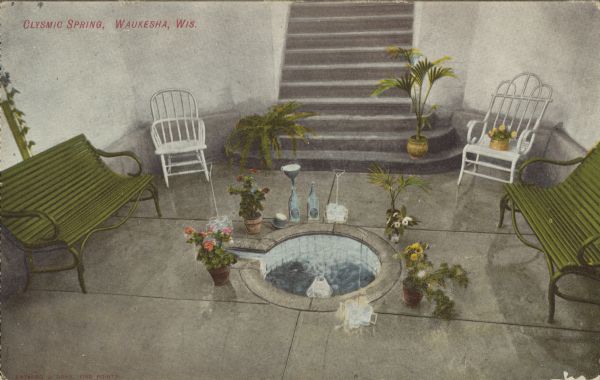 Text on front reads: "Clysmic Spring, Waukesha, Wis." The spring is shown inside a pavilion and surrounded by benches, chairs, flowers and bottles. Between 1868 and 1918, 60 mineral springs were located here. People would travel here to "enjoy the waters."
