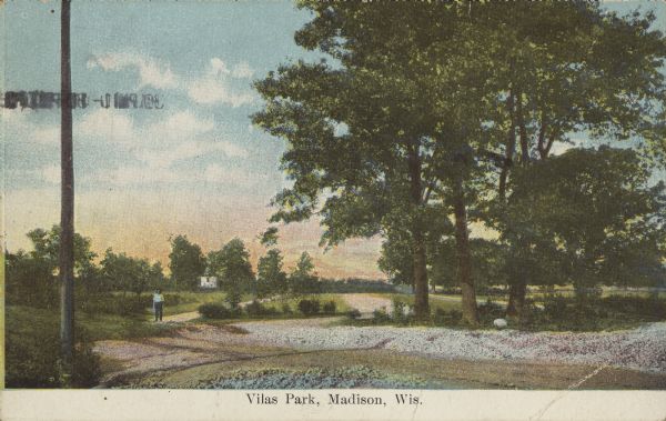 Text on front reads: "Vilas Park, Madison, Wis." A man is standing on a sidewalk next to the shoreline of a lagoon or pond. Sidewalks are surrounded by trees, shrubs and lawns, and a building is in the distance.