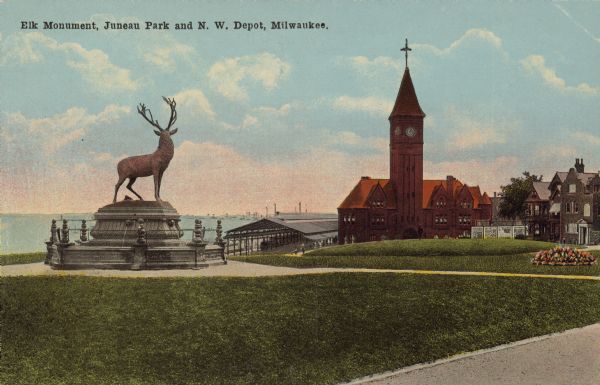 Text on front reads: "Elk Monument, Juneau Park and N. W. Depot, Milwaukee." Statue of an Elk on an elaborate plinth in a park with gardens, lawns and sidewalks. Beyond the park is a train station. In the distance on the left is Lake Michigan.