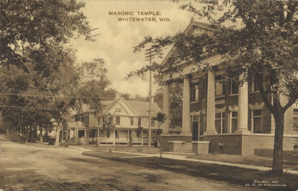 Text on front reads: "Masonic Temple, Whitewater, Wis." A view of the facade and side of a Masonic temple. Four columns support the two-story porch on the neoclassical building and a semi-circular opening appears in the pediment; it may be a part of an enclosed porch or window.