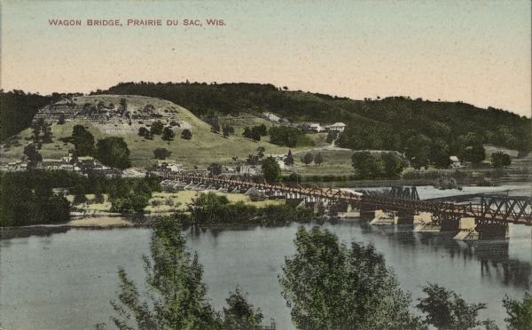 Text on front reads: "Wagon Bridge, Prairie Du Sac, Wis." A long structure over the Wisconsin River. Buildings, bluffs and trees can be seen beyond the far shore.