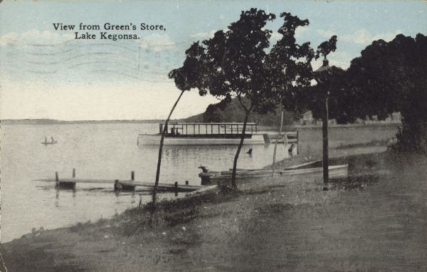Text on front reads: "View from Green's Store, Lake Kegonsa." The shore of Lake Kegonsa, looking over the lake. There are piers, a boathouse, an excursion boat, and more boats pulled up on shore. Two people are in a boat on the water. The far shoreline is in the far distance.