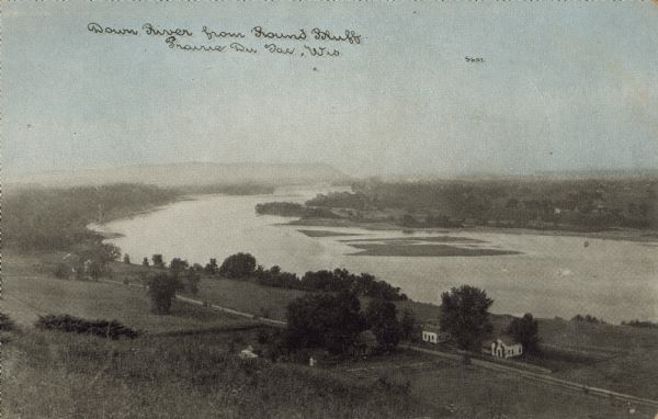 Text on front reads: "Down River from Round Bluff, Prairie Du Sac, Wis." A view of the Wisconsin River with buildings and a road along the left shoreline. Sandbars or islands can be seen in the river and bluffs and trees are in the distance.