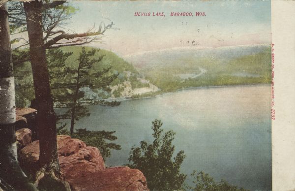 Text on front reads: "Devils [sic] Lake, Baraboo, Wis." An elevated view of the lake from the bluffs. Trees and rocks are on the shoreline.