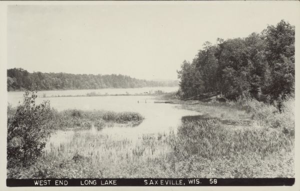 Text on front reads: "West End, Long Lake, Saxeville, Wis." View of a lake with marshland plants in the foreground. A dock, boat and trees are on the right. The far shoreline is covered with trees.