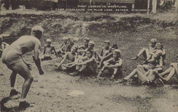 Text on front reads: "First Lesson in Wrestling, Camp Highlands, on Plum Lake, Sayner, Wisconsin." A teacher begins a class in wrestling with a group of students. The private camp for boys was founded in 1904 and was attended by many prominent men.  