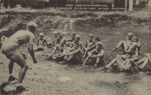 Text on front reads: "First Lesson in Wrestling, Camp Highlands, on Plum Lake, Sayner, Wisconsin." A teacher begins a class in wrestling with a group of students. The private camp for boys was founded in 1904 and was attended by many prominent men.

