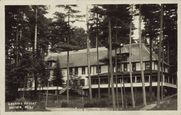 Text on front reads: "Sayners Resort, Sayner, Wis." A large, multi-story, hotel-like resort surrounded by trees. A balcony runs around the main floor, partially covered by a roof.