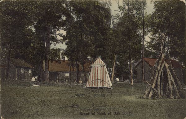Text on front reads: "Beautiful Nook of Oak Lodge." A striped tent is pitched in the center of a clearing in the trees, surrounded by log cabins and a cone shaped pile of logs. The name of the town was changed to Slinger in 1921.