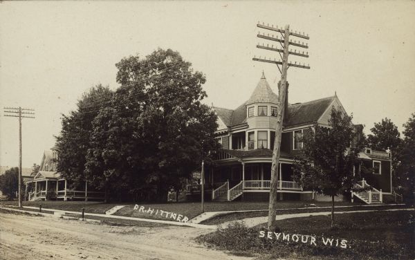 Text on front reads: "Dr. Hittner, Seymour, Wis." The home of a Doctor on an unpaved residential street with sidewalks and trees. Another home is on the left.