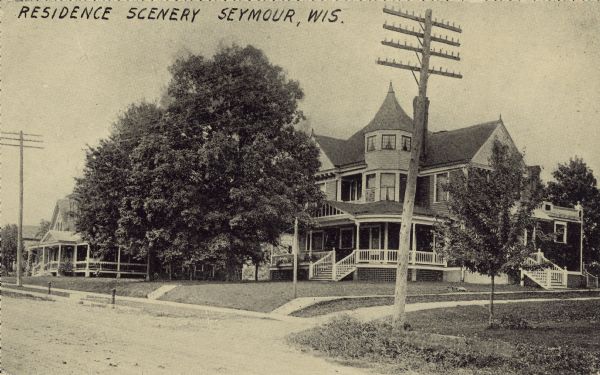 Text on the front reads: "Residence Scenery, Seymour, Wis." Handwritten on the back: "Residence of Dr. Hittner, about the turn of the century, 1900-1910." The home of a doctor on an unpaved residential street with sidewalks and trees. Another home is on the left.