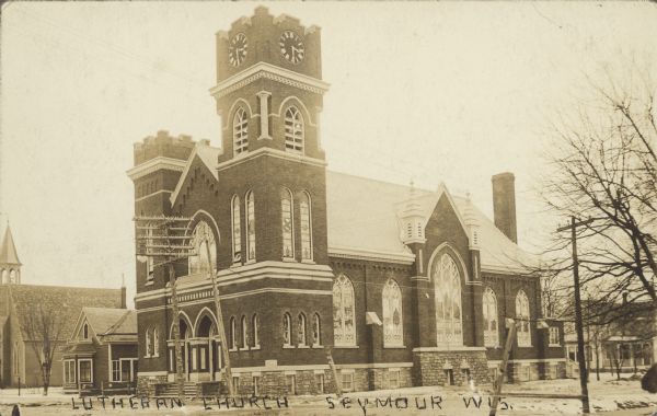 Text on front reads: "Lutheran Church, Seymour, Wis." The Emmanuel Evangelical Lutheran Church was built in 1915 of brick in the Gothic Revival style. There is a clock tower on the right corner of the building.
