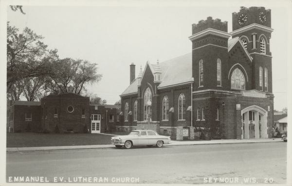 Text on front reads: "Emmanual Ev. Lutheran Church, Seymour, Wis." The Emmanuel Evangelical Lutheran Church was built in 1915 of brick in the Gothic Revival style. An automobile is parked at the curb.