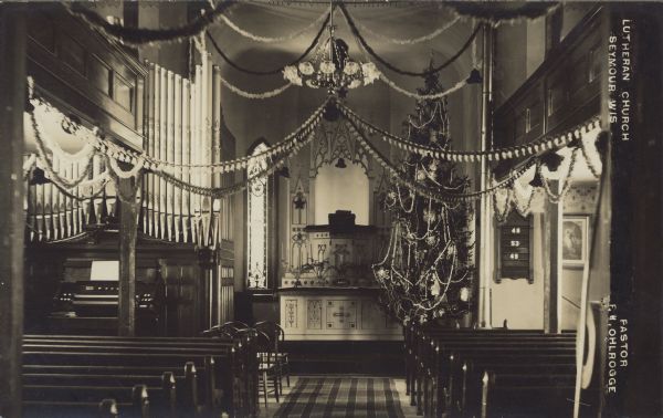 Text on front reads: "Lutheran Church, Seymour, Wis., Pastor, F.W. Ohlrogge." An interior view of the Immanuel Lutheran Church. The Congregation was organized about 1876. The church was built in 1878 with additions added through the years, and the pipe organ was installed in 1904. The church is decorated ornately for Christmas with a very tall tree near the altar.