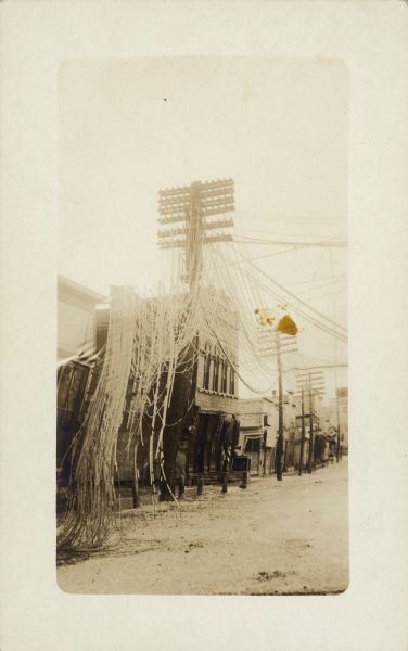 Damage to buildings and wires in a sleet storm. Handwritten on the back: "The after effects of sleet storm in Jan/16 at Seymour, Wis. By the looks of this, the buildings were bent from the sleet effects of the sleet storm. This is only to show you how it looked when all wires came down. Recognize Kahnt's Shoe Store & the crossing we took to the depot?"