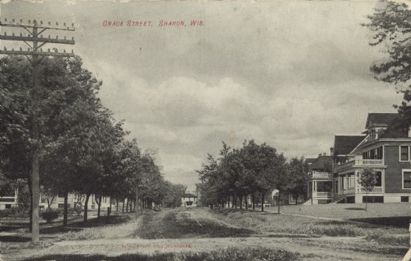 Text on front reads: "Grace Street, Sharon, Wis." A tree-lined, unpaved street with homes on both sides. There are sidewalks and lawns in front of the homes.