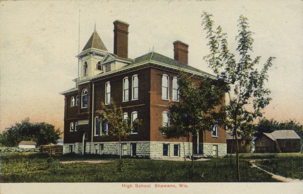 Text on front reads: "High School, Shawano, Wis." The High School building, built of brick and stone, surrounded by a lawn and young trees.