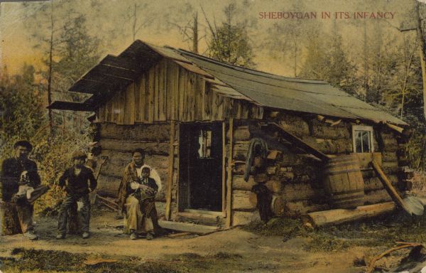 Text on front reads: "Sheboygan in its Infancy." A pioneer family posing in front of their log cabin, sitting on logs. The man has a dog in his lap, the women is holding an infant and a young boy is sitting in the middle. There is a rain barrel on the side of the cabin.