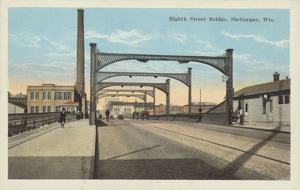 Text on front reads: "Eighth Street Bridge, Sheboygan, Wis." A pedestrian, car and railroad bridge across the Sheboygan River. A bicyclist is coming across the bridge, and automobiles are moving towards the city on the right. Buildings of the city are in the background.