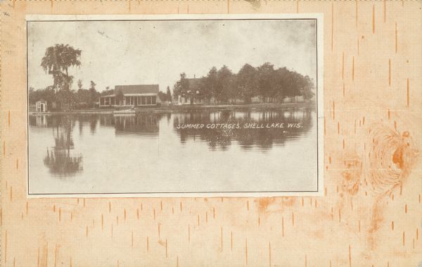 Text on front reads: "Summer Cottages, Shell Lake, Wis." View across lake towards cottages on the shore, and boathouses, piers and trees. A man is standing between the buildings. The image is framed by a pattern of birch bark.