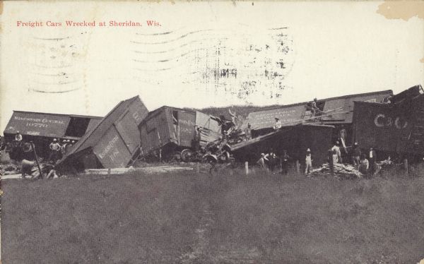Text on front reads: "Freight Cars Wrecked at Sheridan, Wis." A group of people are posing with a line of severely derailed and damaged railroad cars.