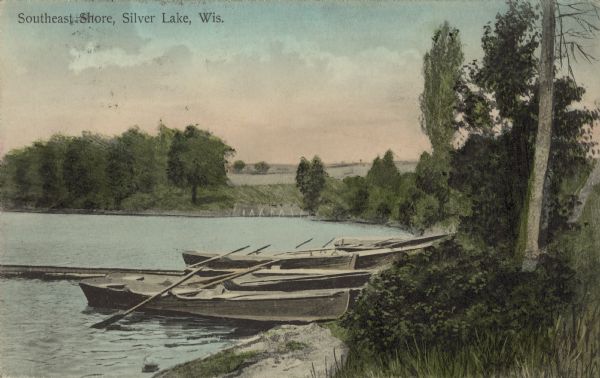 Text on front reads: "Southeast Shore, Silver Lake, Wis." Colorized view of rowboats docked around a pier on the shore of a lake. Chromolithograph.