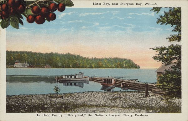 Caption reads: "Sister Bay, near Sturgeon Bay, Wis." and "In Door County 'Cherryland,' the Nation's Largest Cherry Producer." Sister Bay from a rocky beach with a pier, boathouse and boats. This may be Kellstrom's Dock. Buildings can be seen on the far shore. A close-up of cherries has been added to the upper left corner.