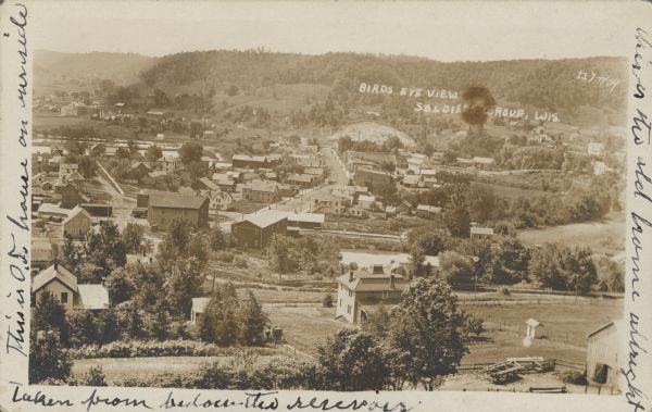 Text on front reads: "Bird's Eye View of Soldiers Grove." View of a small town surrounded by bluffs. The sender has written on both sides of the postcard.