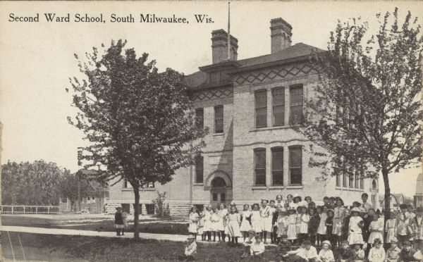 Text on front reads: "Second Ward School, South Milwaukee, Wis." A brick and stone two story schoolhouse with the students posing on the sidewalk in front.