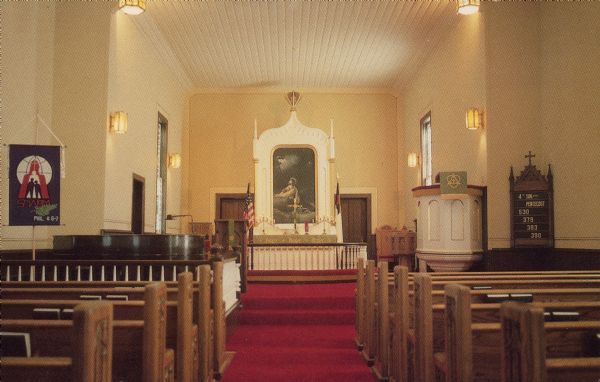Text on the reverse reads: "East Wiota Lutheran Church, South Wayne, Wisconsin 53587. The Oldest Norwegian Lutheran Church in America still in use today. Organized - 1844. Church building started in 1847 - completed in 1851." Interior view of a Lutheran church with tongue-in-groove ceiling, wood pews, wood altar, early 20th century lights, and hand-painted windows.