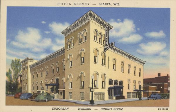 Text on front reads: "Hotel Sydney - Sparta, Wis. European - Modern - Dining Room." View from intersection of a two-story hotel with three-story towers on a street corner. There is a decorative cornice along the roofline. Automobiles are parked at the curb. Other buildings are along the sidewalks on both sides.