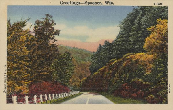 Text on front reads: "Greetings - Spooner, Wis." A country road with a guard fence descends into a valley between tree-covered hills. The trees are showing autumn color.