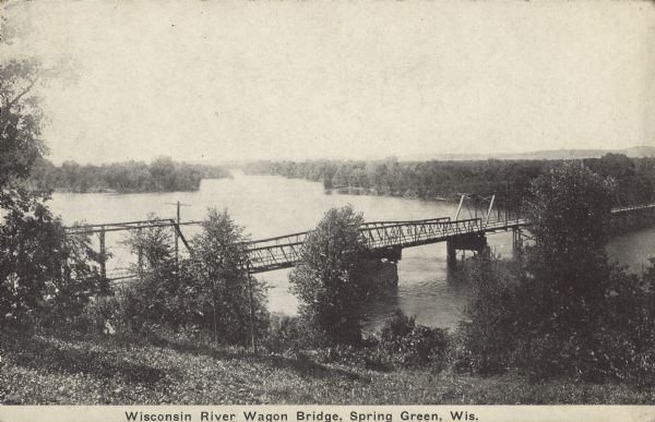 Text on front reads: "Wisconsin River Wagon Bridge, Spring Green, Wis." Elevated view of the bridge over the Wisconsin River on State Highway 23. It was described as a "lost pony truss swing and through truss bridge." A pony truss is not closed at the top. It was replaced in 1965 with a new bridge.