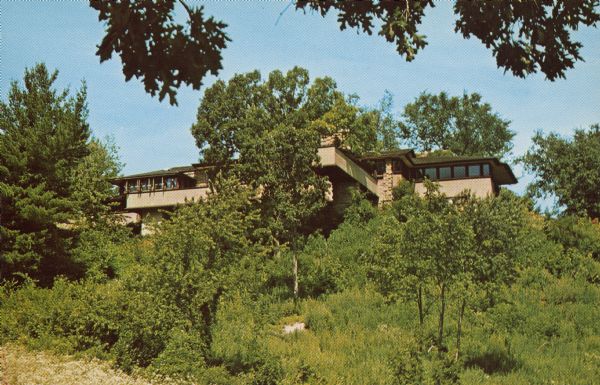 Text on reverse reads: "Taliesin, Spring Green, Wisconsin. Wisconsin office of Taliesin Associated Architects, and campus of the Frank Lloyd Wright School of Architecture, established in 1932 by Mr. & Mrs. Frank Lloyd Wright." Exterior view, looking up towards the house on a hill through the trees.
