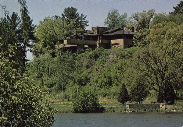 Text on reverse reads: "Taliesin, Home of Frank Lloyd Wright, Spring Green, Wis." View across the pond, looking towards the house on a tree-covered hill. A decorative stone wall with a culvert is on the shoreline of the pond.