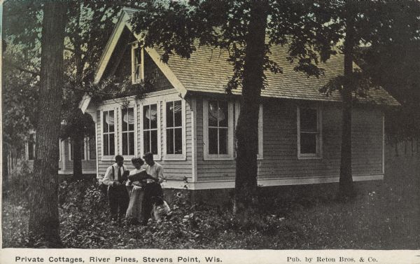 Text on front reads: "Private Cottages, River Pines, Stevens Point, Wis." Two men and a woman stand together in front of clapboard cottages while viewing a newspaper. River Pines Cottage Sanatorium was a private institution for the treatment of tuberculosis. The cottages are surrounded by trees and foliage.


