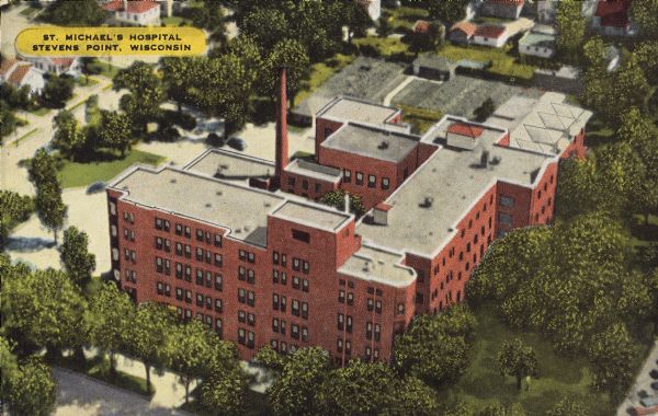 Text on front reads: "St. Michael's Hospital, Stevens Point, Wisconsin." Aerial view of the hospital, built of brick in the Romanesque Revival style in 1927. It is surrounded by trees and a lawn. Additions were later built in 1974 and 1997.