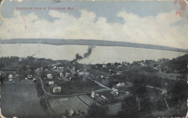 Text on front reads: "Bird's-Eye View of Stockholm, Wis." A village in Pepin County, founded in 1854 by immigrants from Karlskoga, Sweden, who named it after their country's capital. Beyond the village is Lake Pepin on the Mississippi River and Minnesota is on the horizon. Written on the reverse: "That is our house where the cross is."