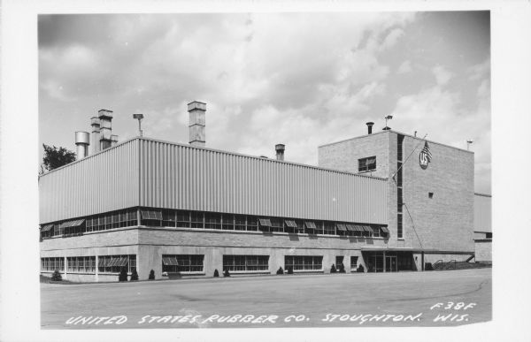 Text on front reads: "United States Rubber Company, Stoughton, Wis." A brick and metal factory building with many windows. Still manufacturing today, Uniroyal Engineered Products manufactures Naugahyde, automotive and custom/specialty products.