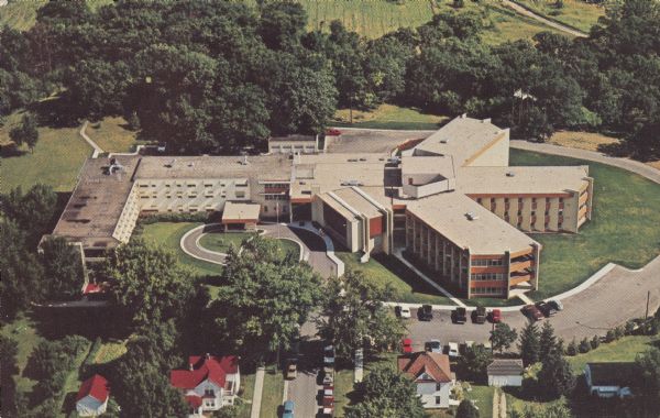 Text on reverse reads: "An aerial view of the Skaalen Sunset Home and the New Addition completed Spring 1971, Stoughton, Wisconsin. The Home has 157 nursing beds, 96 beds for ambulatory residents and 14 residential suites of single or double occupancy. It is owned and operated by 31 Congregations of the American Lutheran Church forming the Skaalen Sunset Home Corporation. Dedicated to Serving the Aging in a Ministry of Mercy in a Christian atmosphere." A large nursing and retirement facility in a wooded setting with a neighborhood in the foreground.