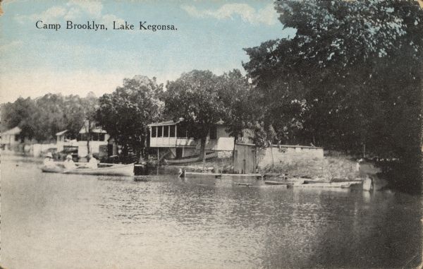 Text on front reads: "Camp Brooklyn, Lake Kegonsa." One man and two women are boating on Lake Kegonsa. Cottages, trees and docks line the shore.