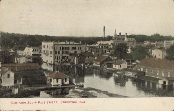 Text on front reads: "View from South Page Street, Stoughton, Wis." An elevated view of the Yahara River as is flows through the town. Many buildings, large and small, are on the banks. A church steeple, clock tower and smokestack are on the horizon.